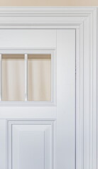 Fragment białych drzwi z frezowanymi opaskami i listwami w środku.
