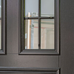 Fragment dębowych drzwi zewnętrznych w kolorze szary antracyt z szybą i szprosami.