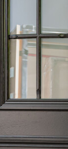 Fragment dębowych drzwi zewnętrznych w kolorze szary antracyt z szybą i szprosami.