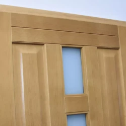 Górny fragment drzwi drewnianych zewnętrznych z płycinami po bokach oraz szybą zespoloną w środku.