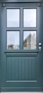 Drzwi drewniane zewnętrzne Drzwi ocieplane zewnętrzne w kolorze RAL 6012 z jedną płyciną imitującą klepkę i czterema szybami. Całość wykończona jest listwami ozdobnymi i gzymsami.