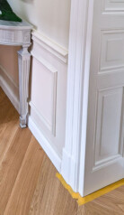 fragment białej drewnianej ościeżnicy płycinowej i ściany z nowoczesną boazerią i listwami przypodłogowymi.